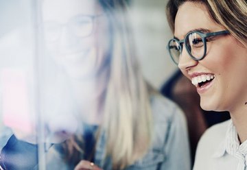 Smiling woman with glasses and longer hair looks at a screen.