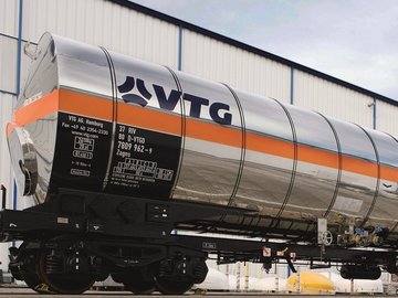 White liquid gas tank car with orange stripe in front of a building.