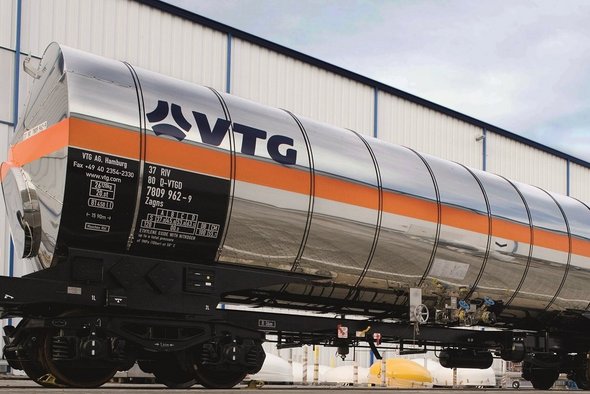White liquid gas tank car with orange stripe in front of a building.