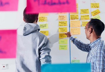 Two employees stick Post-its on a whiteboard 