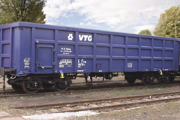 Blue box car on a track in front of green trees.