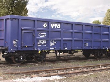 Blue box car on a track in front of green trees.