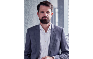 Smiling man in gray suit with brown hair and beard.