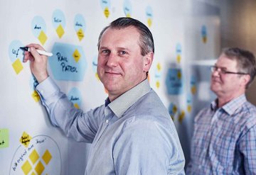 Three male employees are standing in front of a whiteboard on which one of them is writing.