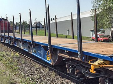 Blue flat car with side elements in front of a gray hall.