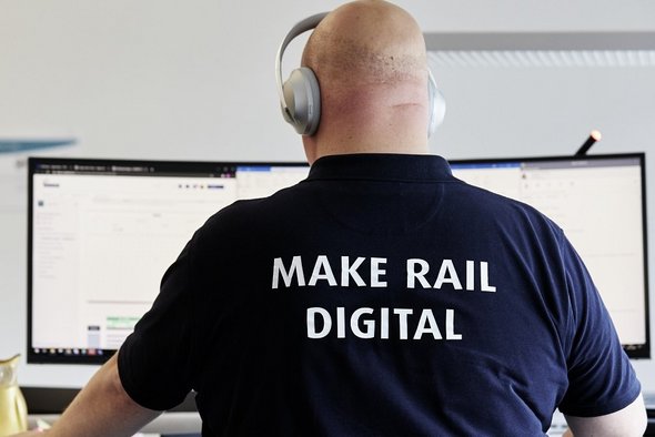 A bald employee wearing headphones sits in front of a screen.