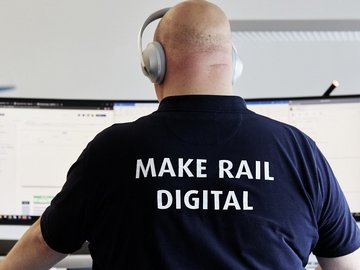 A bald employee wearing headphones sits in front of a screen.