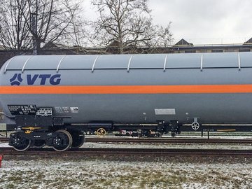 Gray liquid gas tank car with orange stripe and blue logo on a rail.