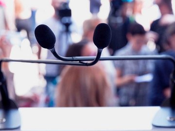 Two microphones in front of a large crowd of listeners.