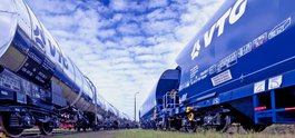 Silvery VTG chemical tank car next to blue VTG standard freight car under blue sky